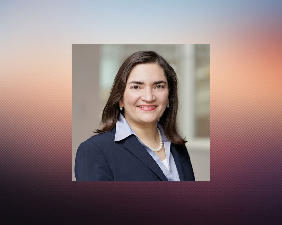 official portrait of Dr. Marcela Maus wearing a dark navy-blue suit jacket, light lavender/purple shirt, and pearl necklace