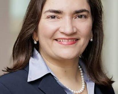 official portrait of Dr. Marcela Maus wearing a dark navy-blue suit jacket, light lavender/purple shirt, and pearl necklace