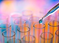 A pipette releases a water droplet into a test tube among an array of other colorful test tubes.