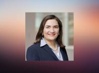 official portrait of Dr. Marcela Maus wearing a dark navy-blue suit jacket, light lavender/purple shirt, and pearl necklace